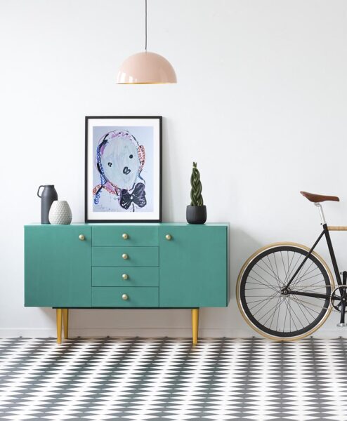 Plant and poster on green cabinet in retro living room interior with bicycle and copy space on the wall