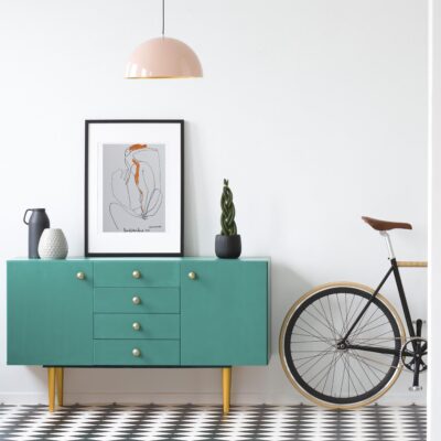 Plant and poster on green cabinet in retro living room interior with bicycle and copy space on the wall