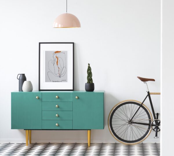 Plant and poster on green cabinet in retro living room interior with bicycle and copy space on the wall