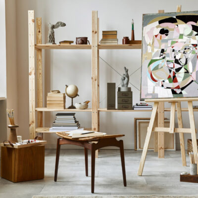 Unique artist workspace interior with stylish teak commode, wooden easel, bookcase, artworks, painting accessories, decoration and elegant personal stuff. Modern work room for artist. Template.