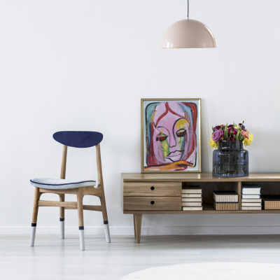 Pink lamp above wooden cupboard with colorful flowers in minimal living room interior with chair