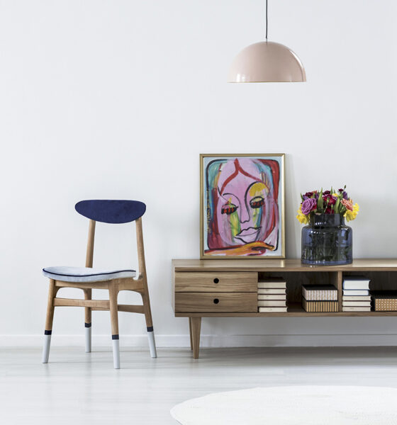 Pink lamp above wooden cupboard with colorful flowers in minimal living room interior with chair
